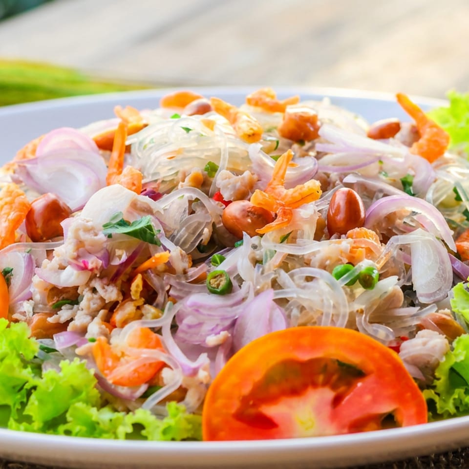 Thai glass noodle salad with shrimp, minced meat, peanuts, onions, tomatoes, chilies, and lettuce garnish on a plate.